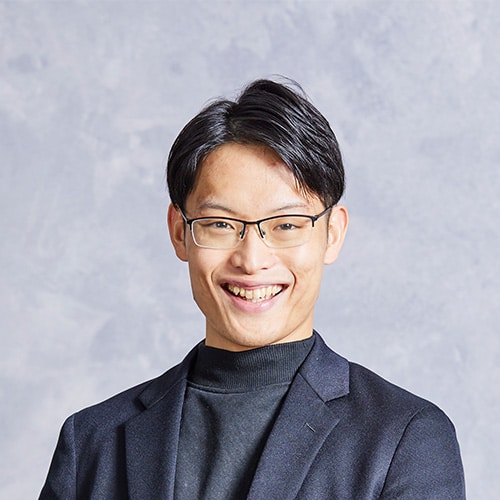 Smiling Asian man with short black hair and glasses, wearing a dark blazer and turtleneck, looking at the camera.