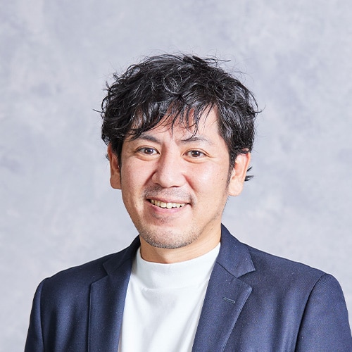 Portrait of a smiling man in a navy blazer and white shirt against a light gray backdrop, a professional headshot.