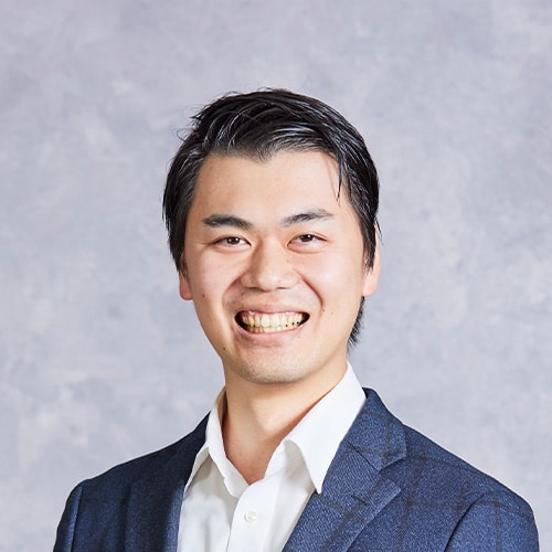 Portrait of a smiling Asian man in a navy blazer and white shirt, looking at the camera against a neutral background.