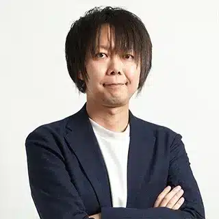 GMOメイクショップ株式会社 千葉 祐輔 部署役職_肩書き クラウドEC営業本部 マーケティングチーム リーダー | テクロ株式会社 Young man with medium-length dark hair, wearing a navy blazer and white shirt, standing with arms crossed and a neutral expression toward the camera.